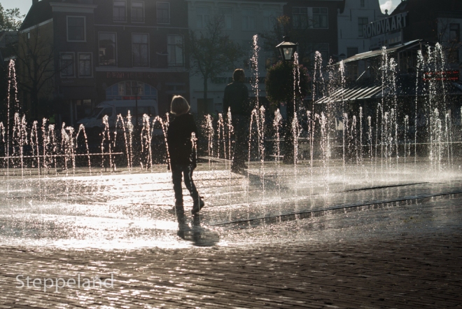 Little Prince following his dad through the sunlit fountain